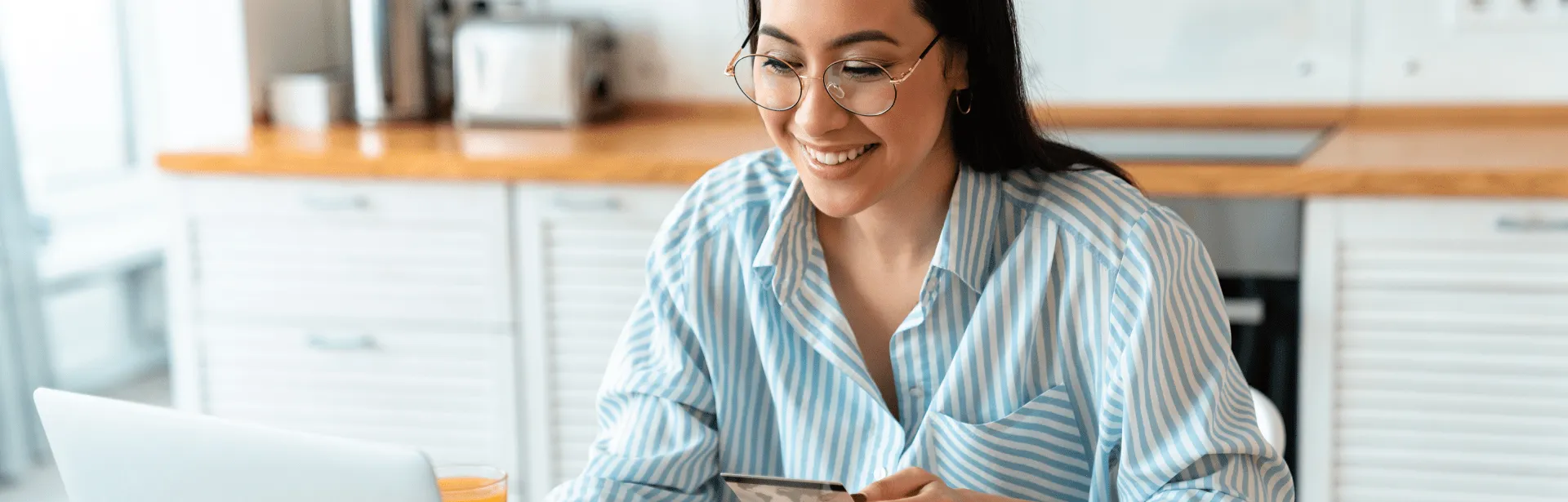 A woman in a kitchen smiling at a computer screen.