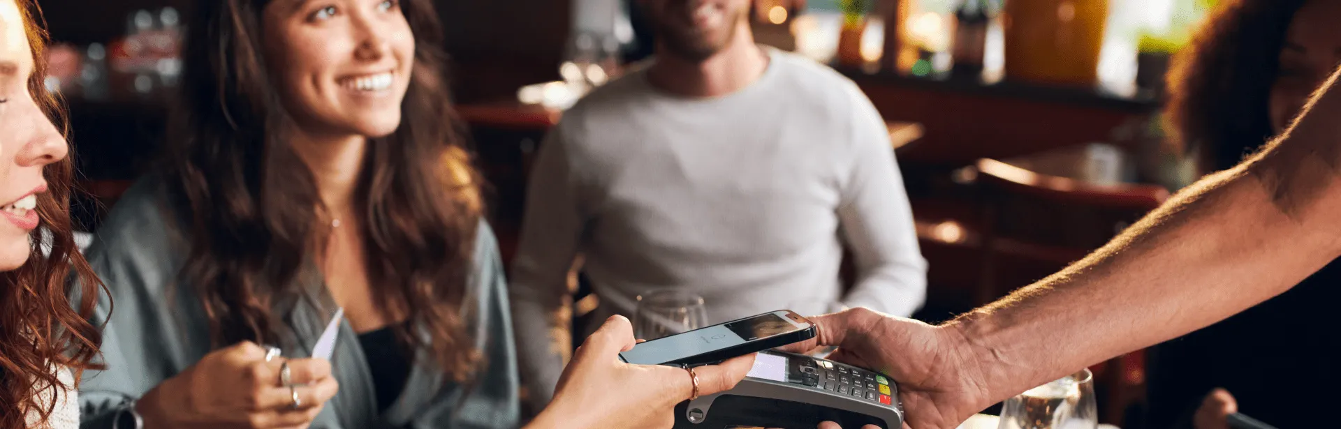 A woman in a restaurant setting using her phone for a tap to pay payment method.